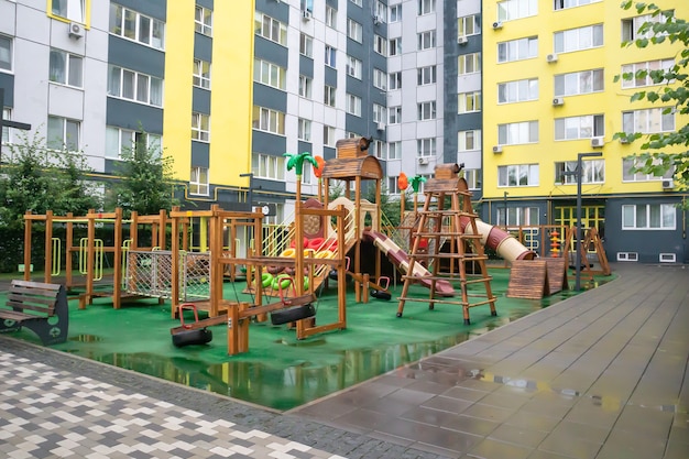 Un cortile di grattacieli con un moderno e grande parco giochi in legno e plastica in una piovosa giornata estiva senza persone. Parco giochi all'aperto vuoto. Un luogo per i giochi e gli sport dei bambini.