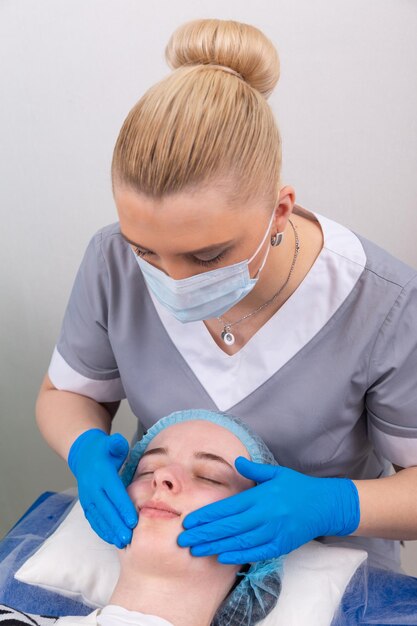 Un cosmetologo femminile tratta manualmente la pelle del paziente con un gel idratante e tonificante