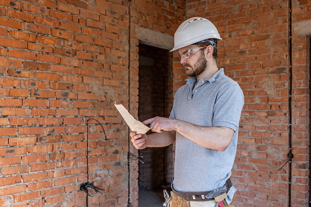 Un costruttore in abiti da lavoro esamina un disegno di costruzione in un cantiere.