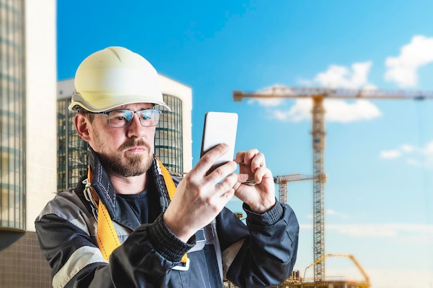 Un costruttore maschio in un elmetto bianco su uno sfondo sfocato di un cantiere edile con un cielo blu Ingegnere civile positivo con la barba