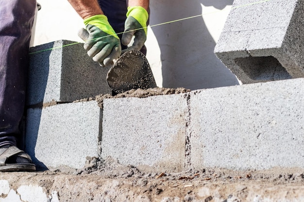 Un costruttore tiene una cazzuola durante la costruzione di un muro fatto di blocchi di cemento aerato