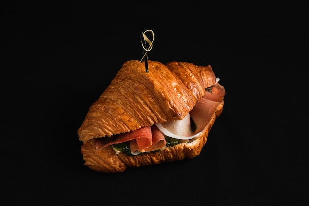 Un croissant con prosciutto e pesto su sfondo nero, scuro e lunatico