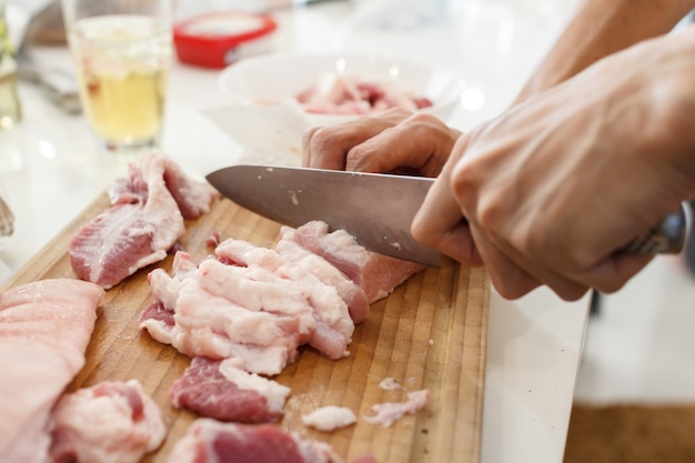 Un cuoco taglia la carne di maiale con un coltello. Concetto di cucina