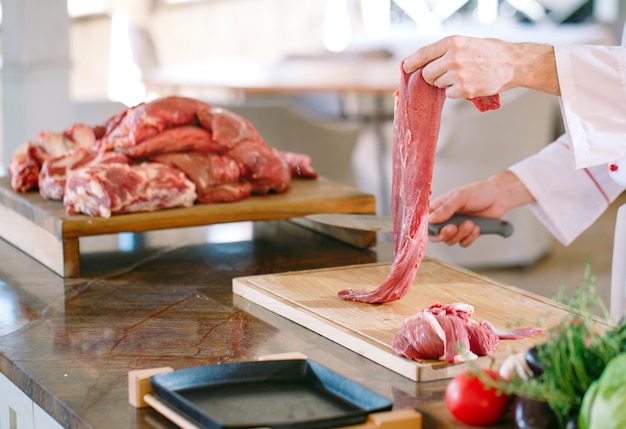 Un cuoco uomo taglia la carne con un coltello in un ristorante.