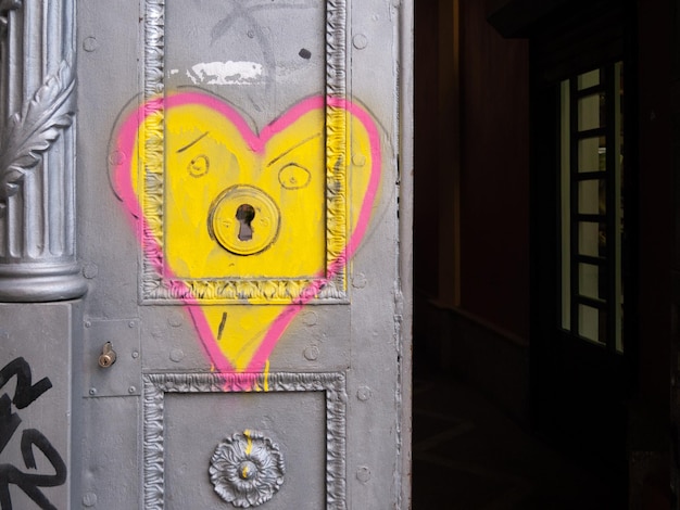 Un cuore con una faccia gialla è dipinto su una porta grigia