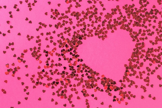 Un cuore creativo composto da un gran numero di piccoli cuori lucidi su sfondo rosa. Il concetto di San Valentino. Disposizione piatta.