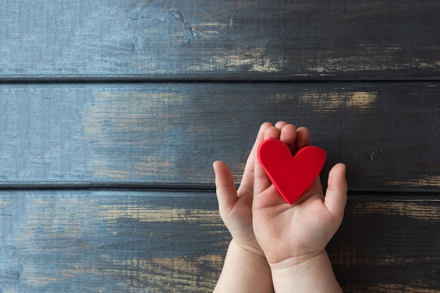Un cuore rosso detenuto da due maniglie per bambini su uno sfondo di legno Concezione d'amore Spazio di copia vista dall'alto
