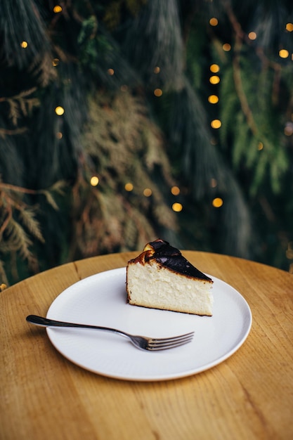 Un delizioso pezzo di cheesecake o torta sul tavolo Sfondo di rami di pino e ghirlande festive