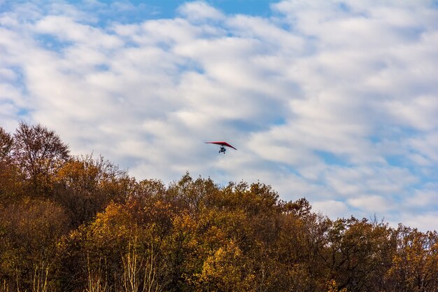 Un deltaplano sorvola una bellissima foresta autunnale contro un cielo azzurro con nuvole