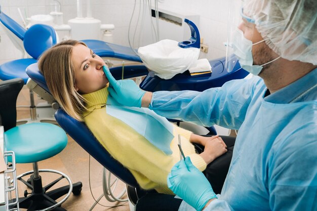 Un dentista che indossa una maschera protettiva si siede accanto al paziente e gli copre la bocca con un dito.