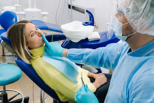 Un dentista che indossa una maschera protettiva si siede accanto al paziente e si copre la bocca con un dito