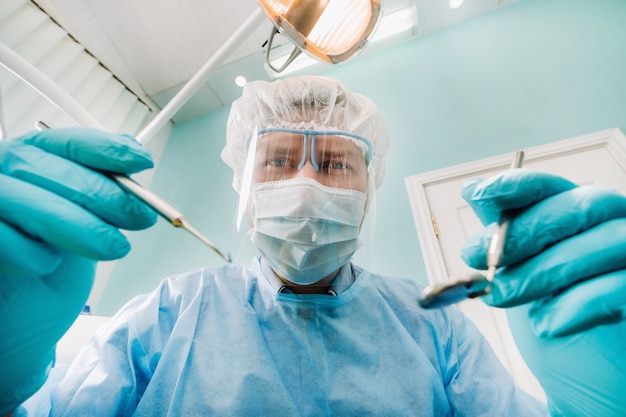 Un dentista che indossa una maschera protettiva si siede nelle vicinanze e tiene gli strumenti in mano prima di curare un paziente nello studio dentistico