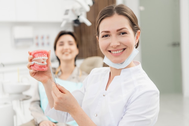 Un dentista femmina sorridente con dentiere nelle sue mani. Nell'ufficio di odontoiatria