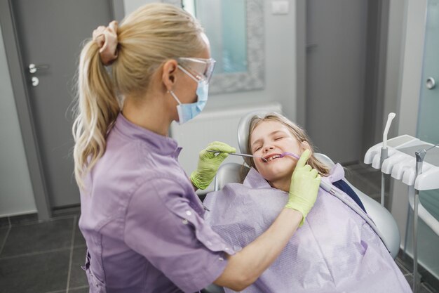 Un dentista femminile che esamina i denti della bambina carina durante la procedura dentale presso l'ufficio del dentista.