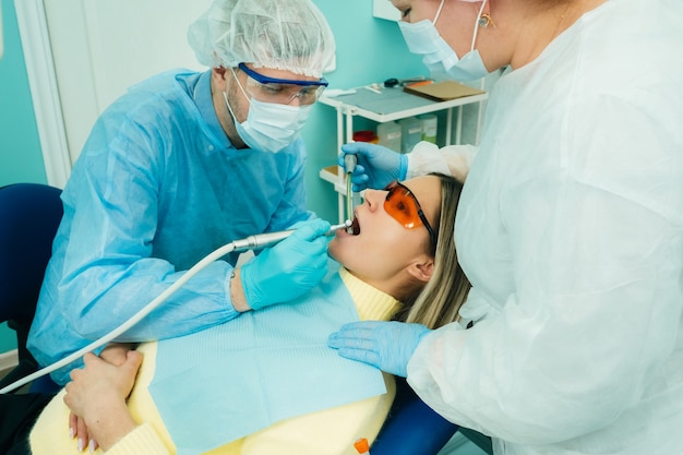 Un dentista maschio con strumenti dentali perfora i denti di un paziente con un assistente. Il concetto di medicina, odontoiatria e assistenza sanitaria.