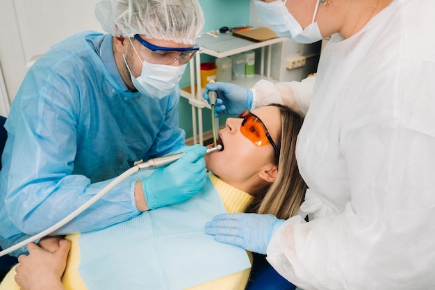 Un dentista maschio con strumenti dentali perfora i denti di un paziente con un assistente. Il concetto di medicina, odontoiatria e assistenza sanitaria.