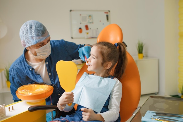 Un dentista maschio insegna a una bambina come lavarsi i denti correttamente con uno spazzolino da denti