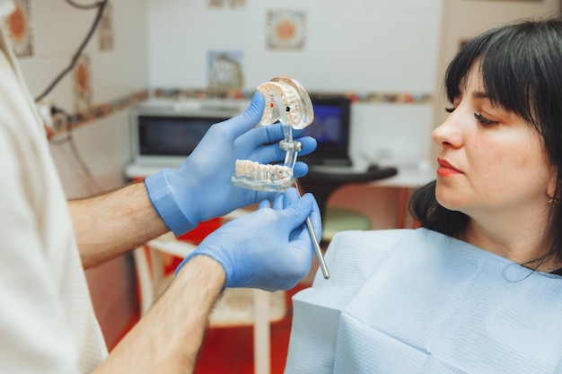 Un dentista ortodontista maschio mostra una mascella di plastica artificiale di un paziente seduto su una poltrona del dentista trattamento medico dello smalto