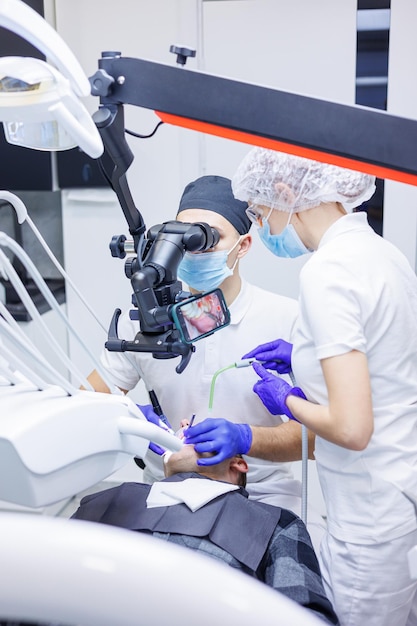 Un dentista tratta i denti utilizzando un microscopio dentale e strumenti L'assistente tiene una siringa con aria e acqua Studio dentistico