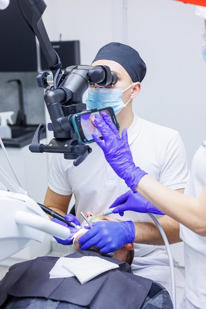 Un dentista tratta i denti utilizzando un microscopio dentale e strumenti L'assistente tiene una siringa con aria e acqua Studio dentistico