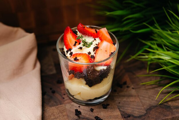 Un dessert cremoso con fragole e cioccolatini in un bicchiere su uno sfondo di legno