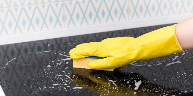 Un detergente con un guanto giallo lava un utensile da cucina con schiuma detergente e una spugna