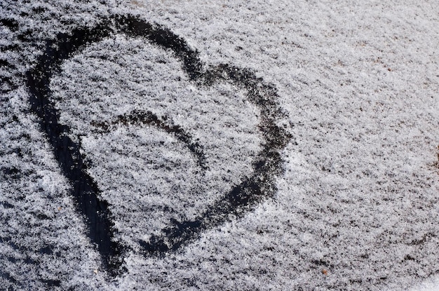 Un disegno a forma di cuore sulla neve caduta sul vetro dell'auto