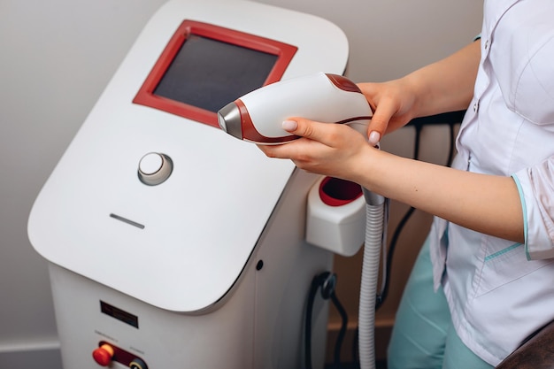 Un dispositivo medico bianco in piedi in un salone di bellezza. Una donna in uniforme tiene tra le mani ascetica per mettersi al lavoro. Lavorare con un dispositivo per il trattamento della pelle del viso. Il concetto di salute.