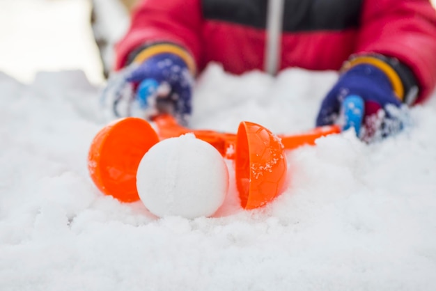 Un dispositivo per scolpire palle di neve nelle mani dei bambini sullo sfondo della neve Giochi invernali dei bambini con le palle di nevi