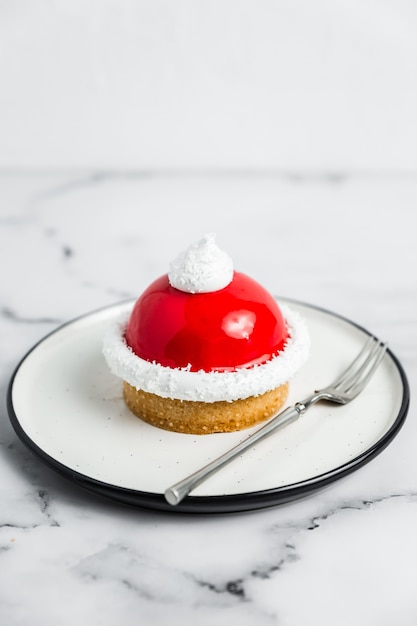 Un dolce di tartelette di mousse rossa e bianca su un piatto bianco, una forchetta da dessert