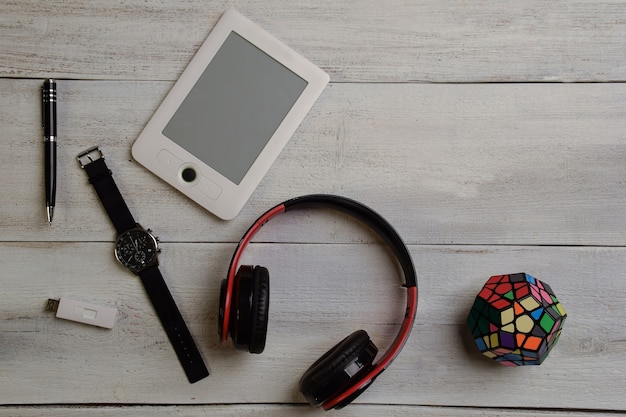 Un e-book, un orologio da polso, un cubo di Rubik, cuffie e una penna giacciono su un tavolo di legno beige.