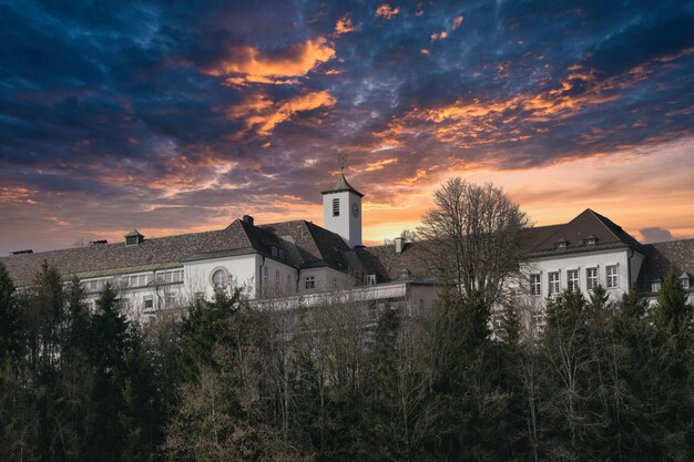 un edificio con una torre in cima è circondato da alberi e un cielo nuvoloso