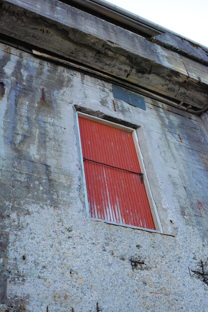 Un edificio in pietra con una porta rossa su una vecchia proprietà deserta Dettagli architettonici dell'esterno di una struttura industriale grigia Pareti in cemento stagionato con una porta di legno alta