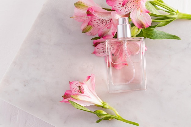 Un'elegante bottiglia di profumo cosmetico o spray appoggiata su un ramo di fiori rosa primaverili presentazione del prodotto bottiglia senza nome