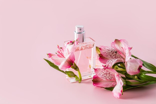 Un'elegante bottiglia di profumo femminile o acqua di toletta su uno sfondo rosa con delicati fiori di astromeria una copia della presentazione dell'aroma spaziale