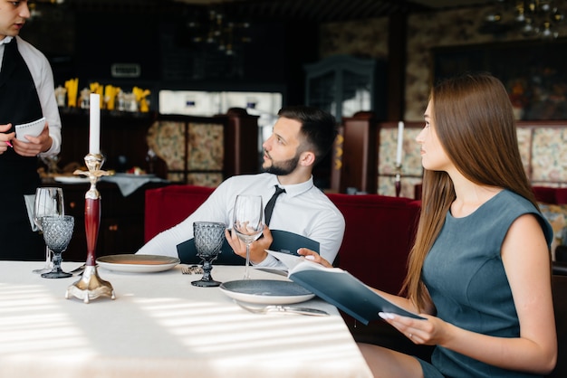 Un elegante cameriere serve una giovane coppia che è venuta ad un appuntamento in un ristorante gourmet. Servizio clienti nella ristorazione.