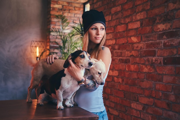 Un'elegante donna bionda tatuata in maglietta e jeans abbraccia due simpatici cani.