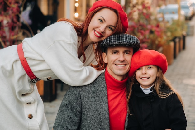 Un'elegante famiglia di tre persone passeggia per la città autunnale posando per un fotografo Papà, mamma e figlia nella città autunnale