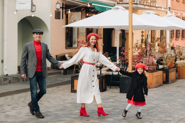 Un'elegante famiglia di tre persone passeggia per la città autunnale posando per un fotografo Papà, mamma e figlia nella città autunnale