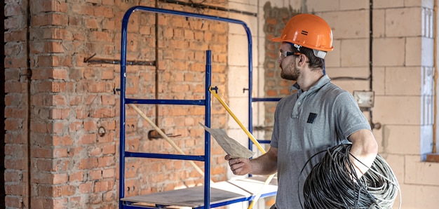 Un elettricista esamina un disegno costruttivo mentre tiene in mano un cavo elettrico in un cantiere.