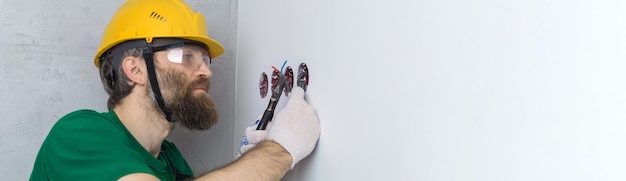 Un elettricista installa le prese nell'appartamento Un ragazzo con un casco arancione e una tuta fa l'impianto elettrico in casa