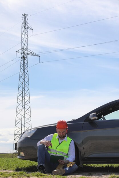 Un elettricista nei campi vicino alla linea di trasmissione di potenza. L'elettricista gestisce il processo di costruzione delle linee elettriche. Il meccanico in un casco e guanti speciali di forma riflettente sul lavoro.