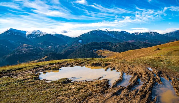 Un'enorme pozza fangosa con fango disgustoso su un piccolo sentiero nelle montagne dei Carpazi sullo sfondo di splendide colline autunnali