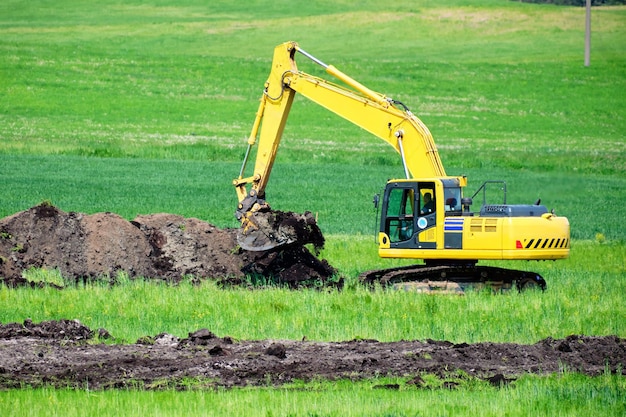 Un'escavatore mentre scava una trincea in un campo verde