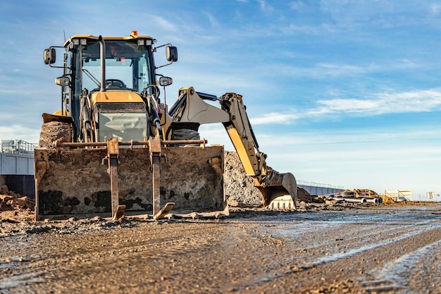 Un escavatore universale sta lavorando in un cantiere contro un cielo nuvoloso Lavori di sterro in un cantiere Moderne attrezzature per movimento terra L'appaltatore sta facendo lavori di costruzione