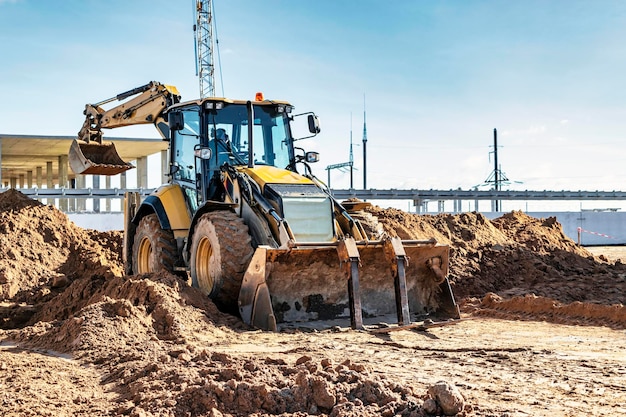 Un escavatore universale sta lavorando in un cantiere contro un cielo nuvoloso Lavori di sterro in un cantiere Moderne attrezzature per movimento terra L'appaltatore sta facendo lavori di costruzione