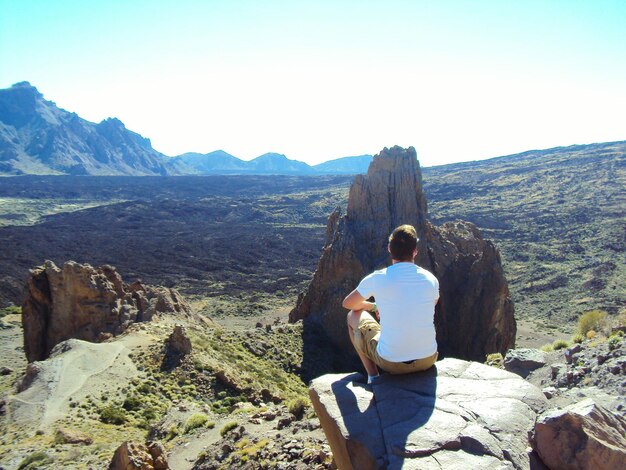 Un escursionista che guarda la montagna seduto su una roccia contro un cielo limpido durante una giornata di sole