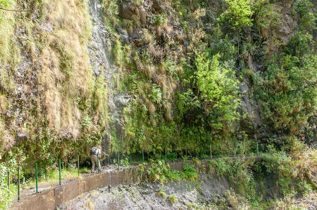 Un escursionista passa sotto una cascata sul sentiero lungo una levada sull'isola di Madeira