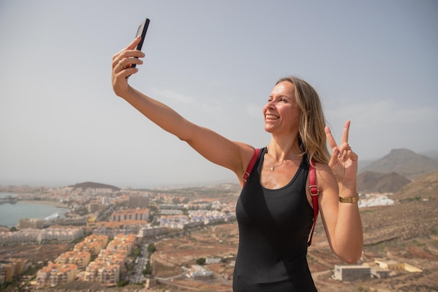 Un'escursionista si scatta un selfie sorridendo in cima alla montagna in estate