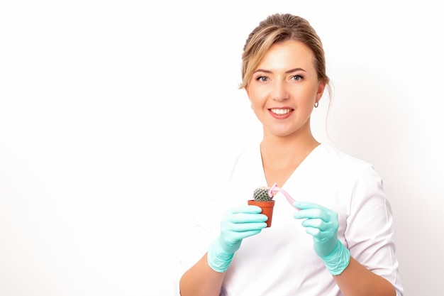 Un'estetista sorridente tiene un piccolo cactus verde con il rasoio nella depilazione della sua mano